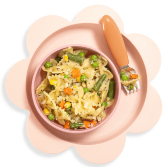 Pink flower kids plate with a pink bowl of pasta and veggies with a baby spoon resting next to it.