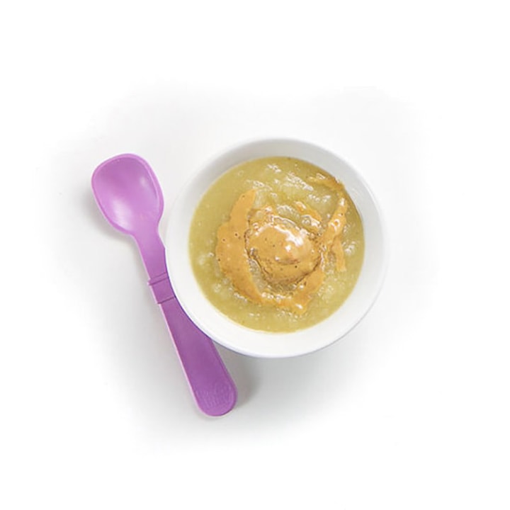 Small baby bowl with purple spoon with apple puree and drizzle of almond butter.