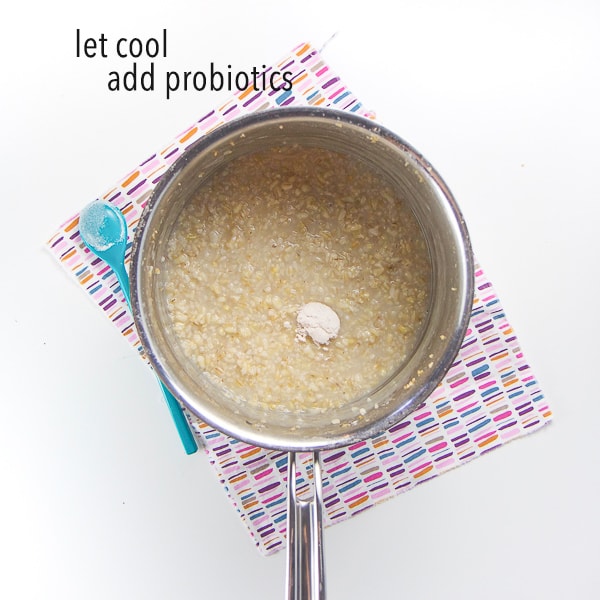 silver saucepan has the three grains cooked and the probiotics on top, read to get mixed in. Words on photo say - let cool, add probiotics