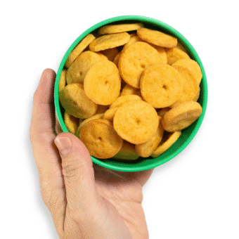 My hand holding a green kids bowl full of round cheese crackers over a white background.
