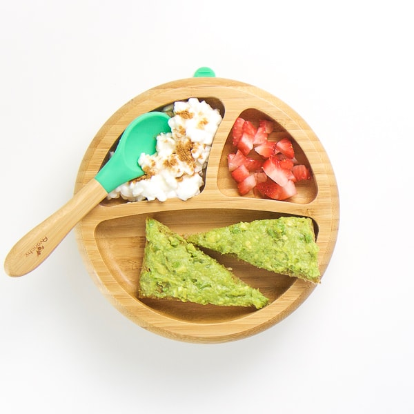 baby-led weaning breakfast on wooden plate with 3 sections - avocado toast, cut strawberries and cottage cheese with cinnamon