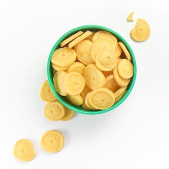 small green bowl filled with round cheese crackers, some are spilling onto the white surface.