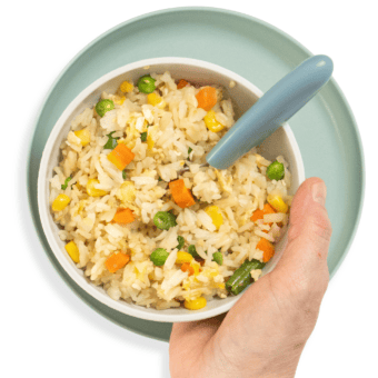 Hand holding blue kids bowl full of fried rice with veggies.
