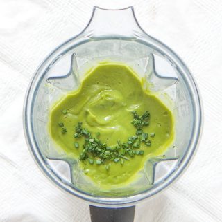 blender on top of a white tablecloth filled with green baby food recipe of broccoli and chives with chopped chives sprinkled on top.