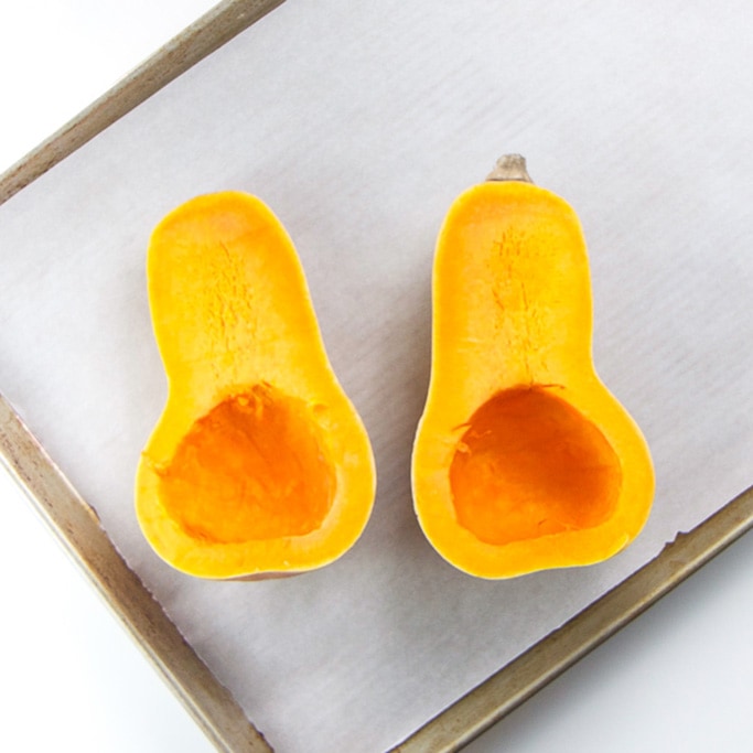 butternut squash but in half on top of a baking sheet sitting on a white background