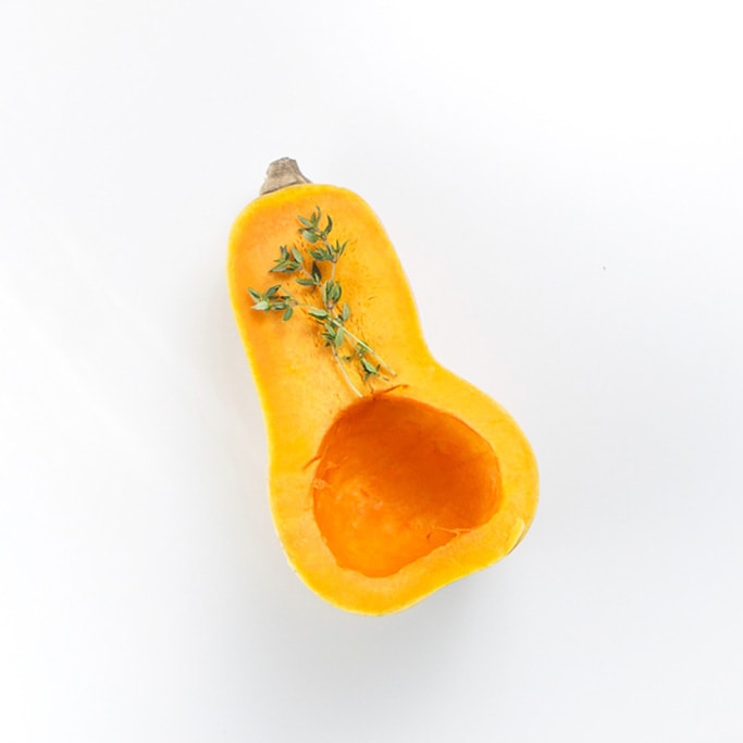 cut butternut squash on a white background with a twig of thyme laying on top of it