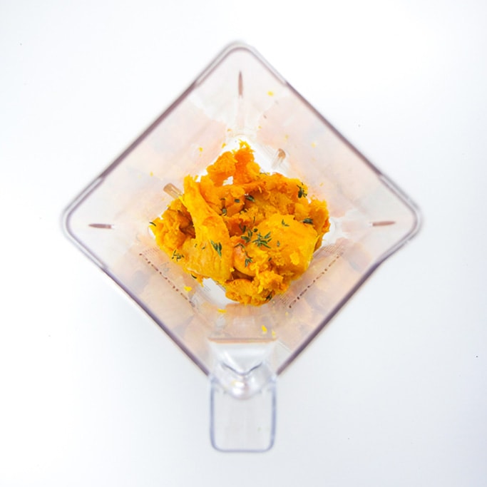 overhead shot of a blender with the cooked butternut squash and thyme inside.
