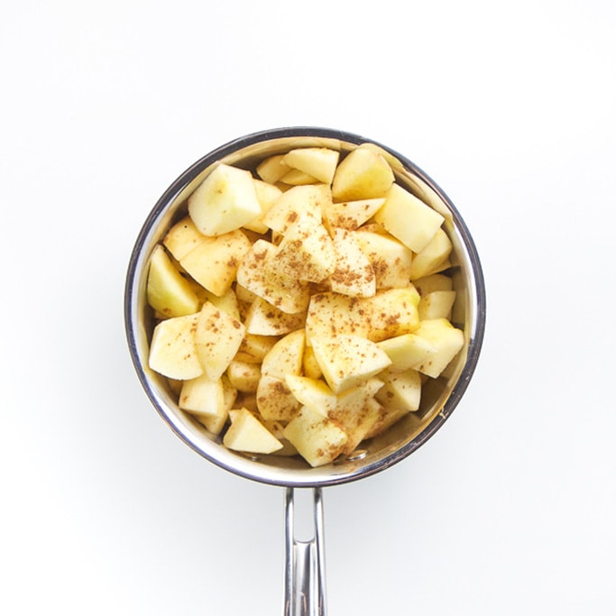 silver saucepan sitting on a white background filled with chunks of apple and a sprinkle of ground cloves
