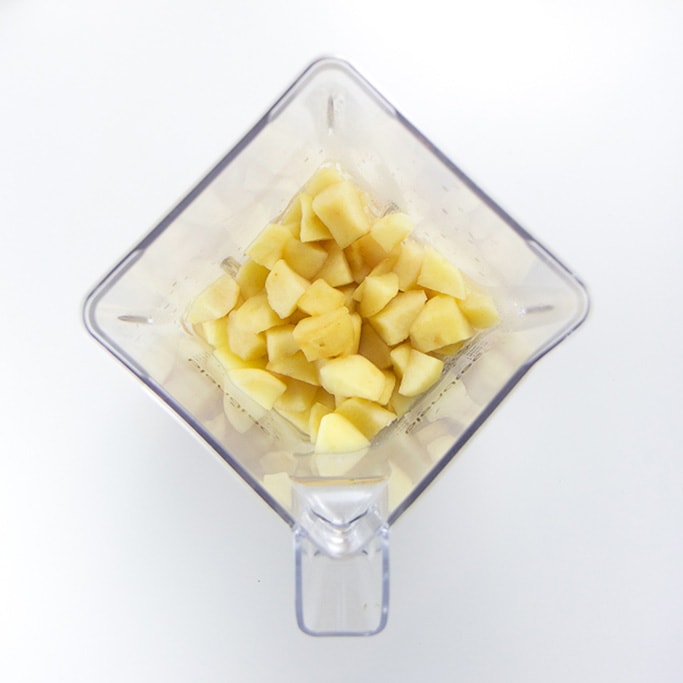 overhead shot of a blender on a white background filled with cooked chunks of apples