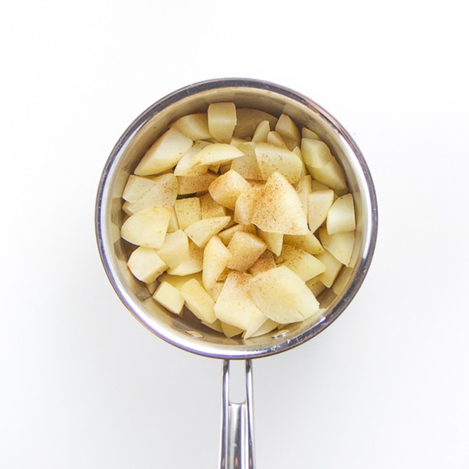 a silver saucepan filled with simmered pear chunks with a clove.