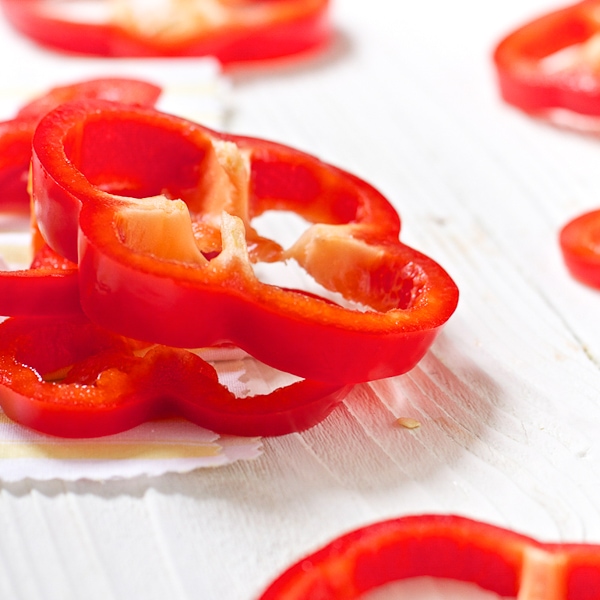 slices of red peppers on top of a white wooden board. 
