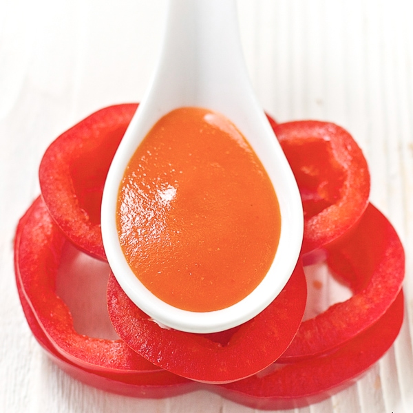 white spoon resting on top of a stack of red pepper slices. spoon has red pepper baby food recipe in it. 