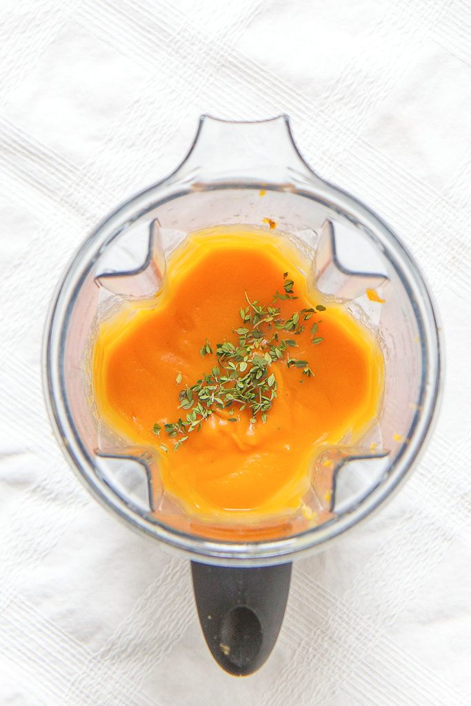  is a top view of a blender filled with sweet potato puree with a sprinkle of thyme on top - baby food for 4 months and up. 