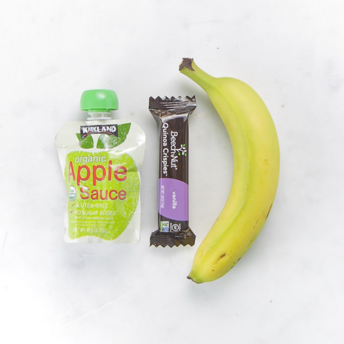 toddler snacks - apple sauce, quinoa bar and banana on a white surface. 