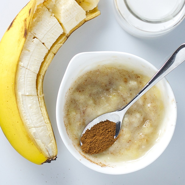 A small white bowl filled with a banana baby food puree with a spoon resting on top filled with cinnamon. 