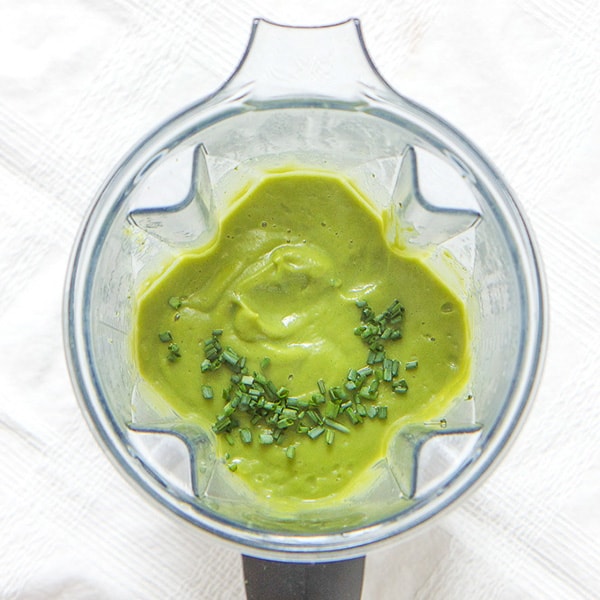 A clear blender filled with a creamy broccoli baby food puree sprinkled with chives on top.