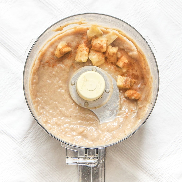 A food processor is filled with banana puree and has chunks of banana and cinnamon on top. 