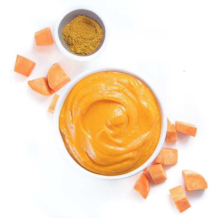 A bowl of sweet potato baby food puree with chunks of sweet potato and a bowl of curry powder next to it.
