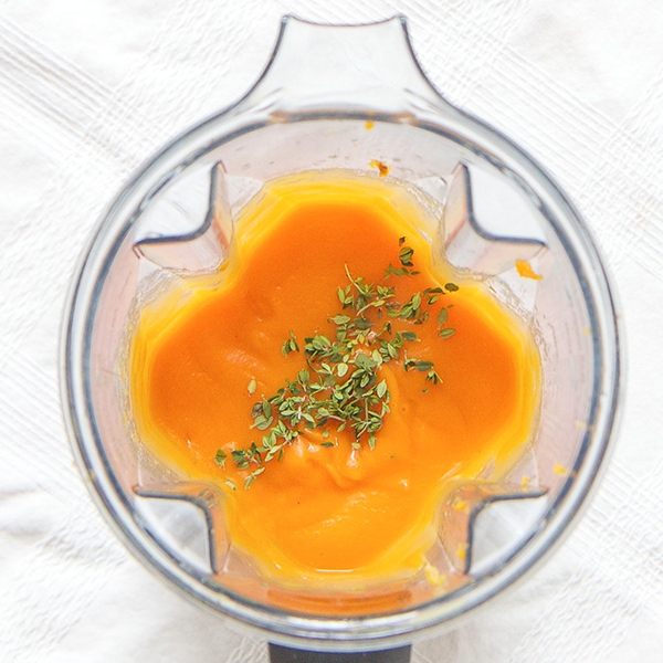 A clear blender is filled with a smooth sweet potato puree with a sprinkle of thyme on top. 