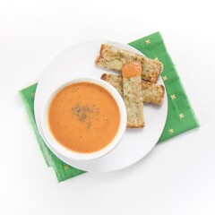 small white bowl filled with an easy creamy tomato soup is sitting on a white plate with 3 cheesy dippers next to the bowl. The bowl is on a green napkin sitting on a white surface.