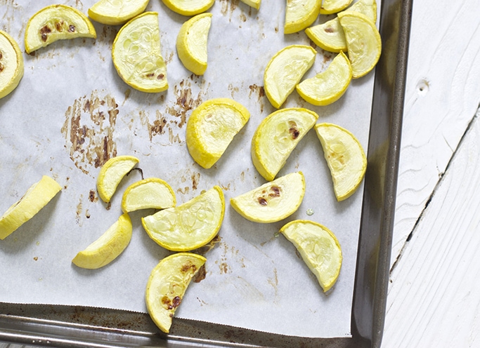 On a white parchment paper lined baking sheet are cut up and roasted yellow squash chunks.