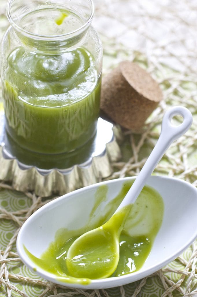 A jar filled with a green smooth zucchini baby food puree with a small bowl in front of the jar filled with the puree that is scraped clean. 