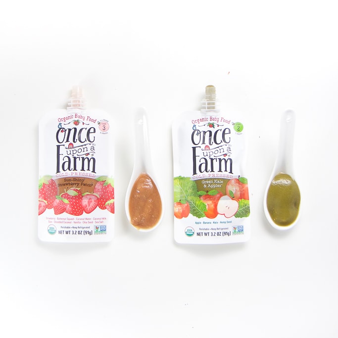2 organic once upon a farm baby food pouches with spoons next the them with puree inside.
