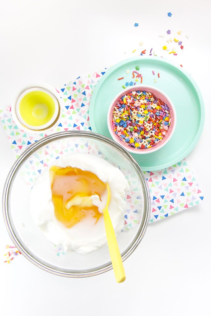 clear bowl with yogurt and honey, with another bowl filled with sprinkles off to the side.