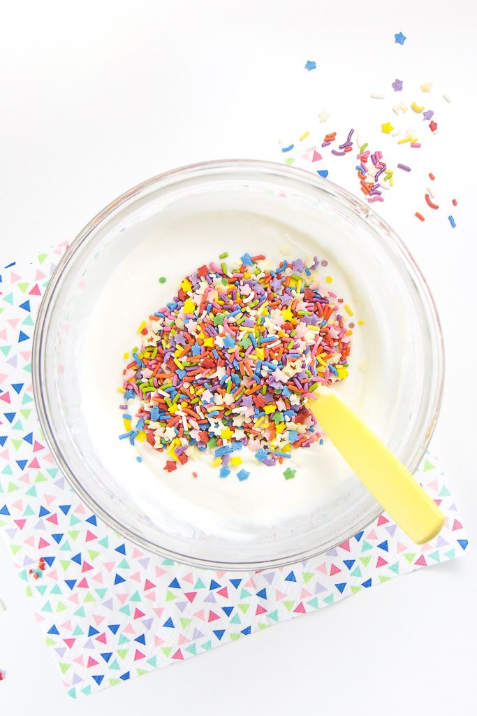 Everything you need to make healthy funfetti popsicles for toddlers and kids - a clear bowl filled with yogurt mixed with honey and a bunch of sprinkles on top.
