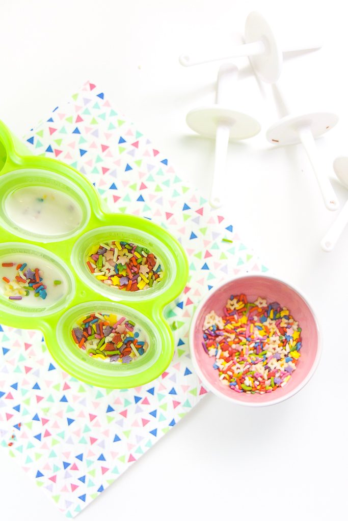 Popsicle molds filled with funfetti yogurt with a sprinkles on top of them.