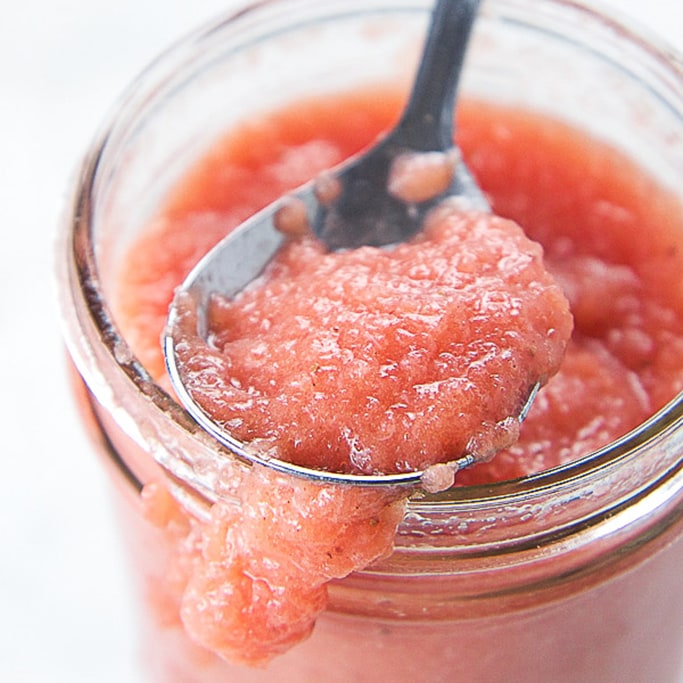 A glass jar filled with strawberry applesauce. 