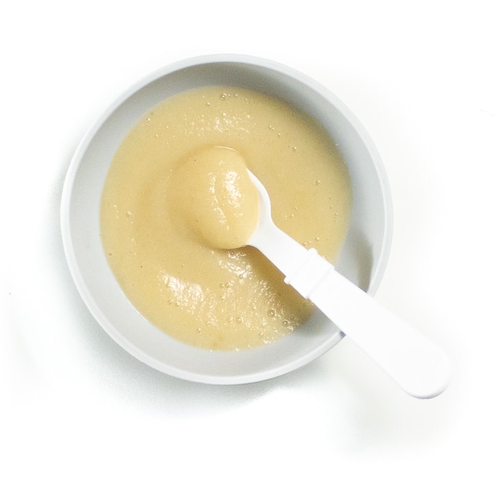 Bowl of pear baby puree with white spoon ready to feed baby. 