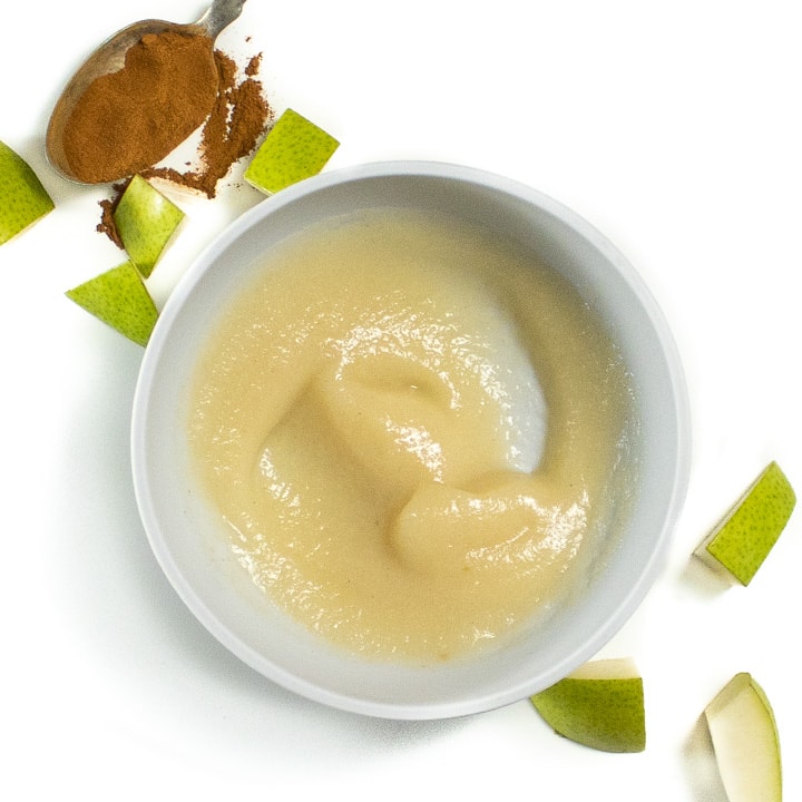pear baby food puree in a gray bowl for baby surrounded by chopped pears and cinnamon.