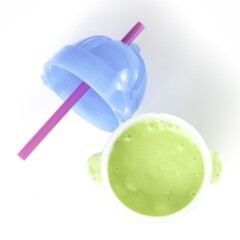 Clear sippy cup filled with a green avocado smoothie for baby and toddler sitting on a white surface.