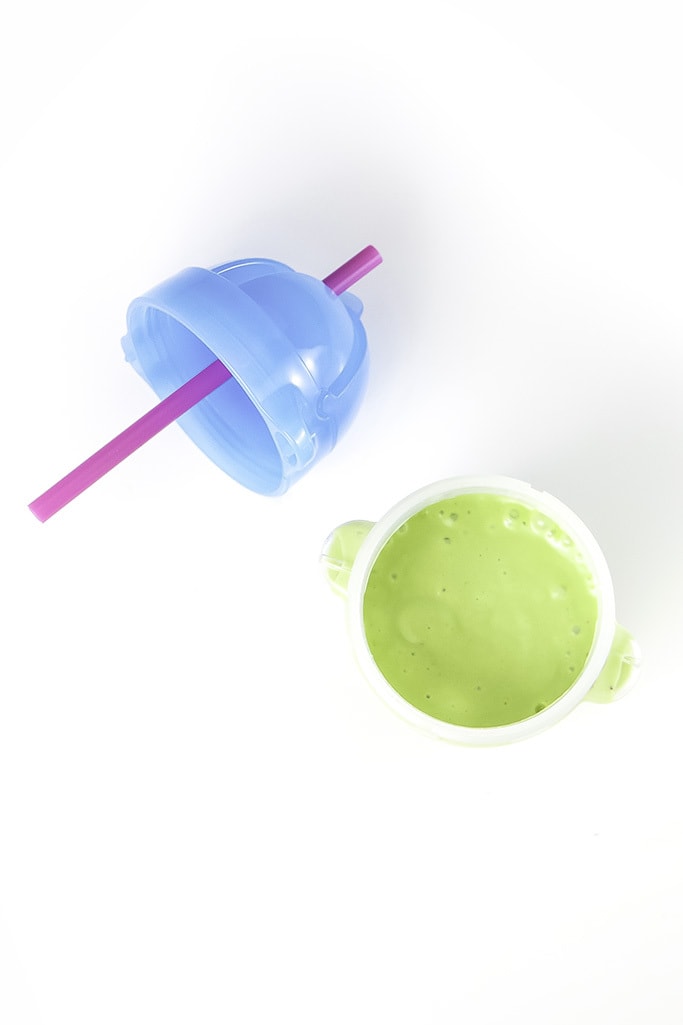 Clear sippy cup filled with a green avocado smoothie for baby and toddler sitting on a white surface. 