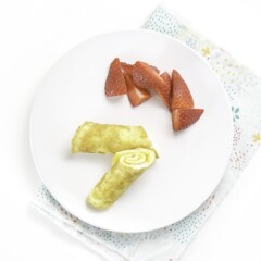 A round white plate with 2 easy-cheesy egg roll-ups on top with some chopped strawberries.