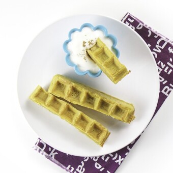 Overhead photo of one white place with 3 pumpkin waffle dippers laying next to a small cup of yogurt.