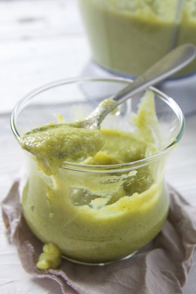 A glass jar filled with a creamy broccoli and asparagus baby food puree. 