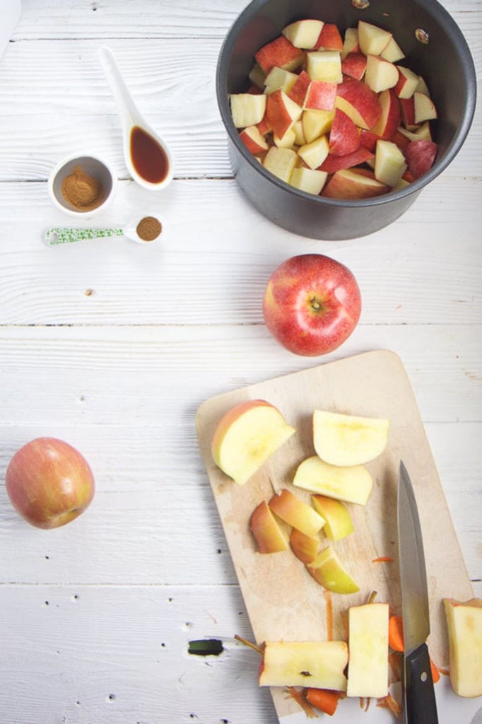 Fresh apples and carrots are getting cut on a cutting board and tossed into a saucepan.