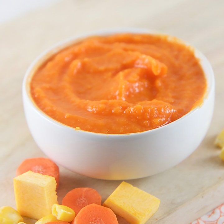Small white bowl filled with pumpkin , squash and corn baby food recipe.