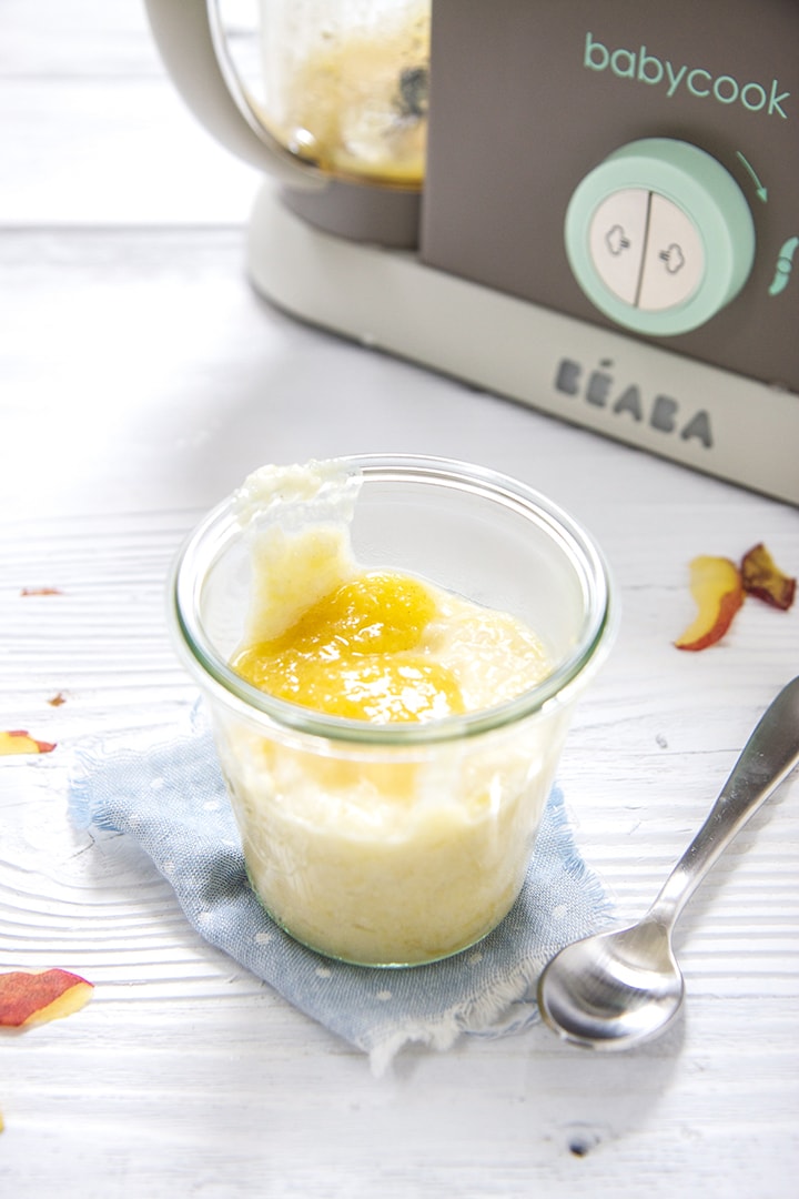 Small glass jar filled with rice pudding and peach puree sitting in front of a Beaba baby food making machine. 