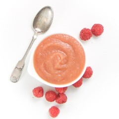 small white bowl filled with a smooth homemade baby food puree with raspberries scattered around it.