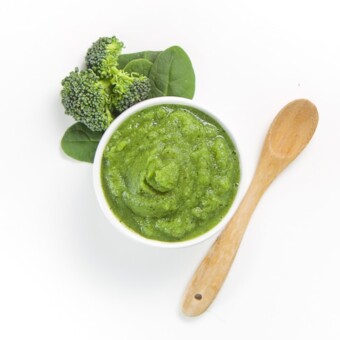 small white bowl filled with homemade green puree with produce and spoon on the white background.