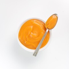 Small white bowl with spoon resting on top with homemade baby food puree inside.