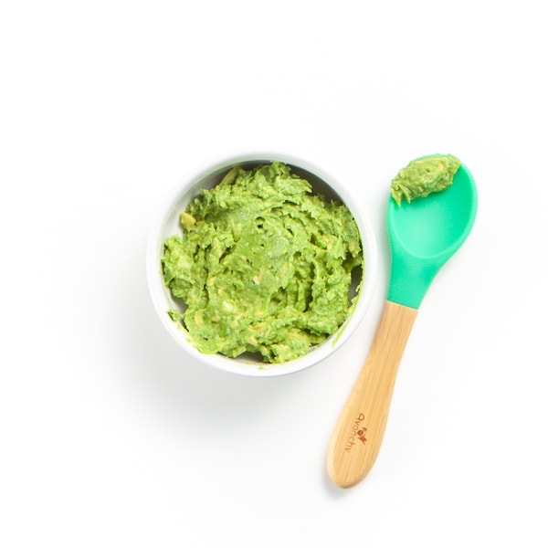 Smashed avocado in a small bowl with spoon resting next to it with puree on it.
