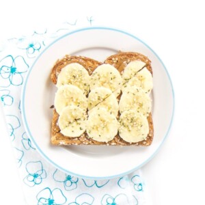 Almond Butter toast with bananas and hemp sprinkles sitting on a round plate.