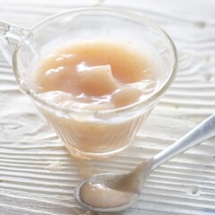 Small glass jar with a spoon resting in front filled with a soft pink baby food puree.