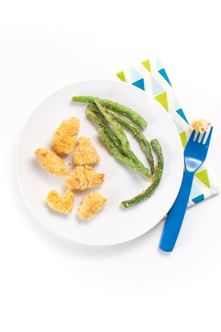 Round plate with chicken nuggets and green beans. Fork on napkin with piece of chicken on it.