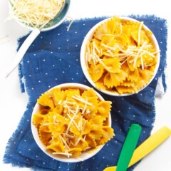2 small bowls filled with pumpkin pasta with 2 kids forks on a blue napkin.