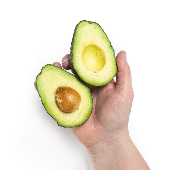 Hand holding a cut open avocado.